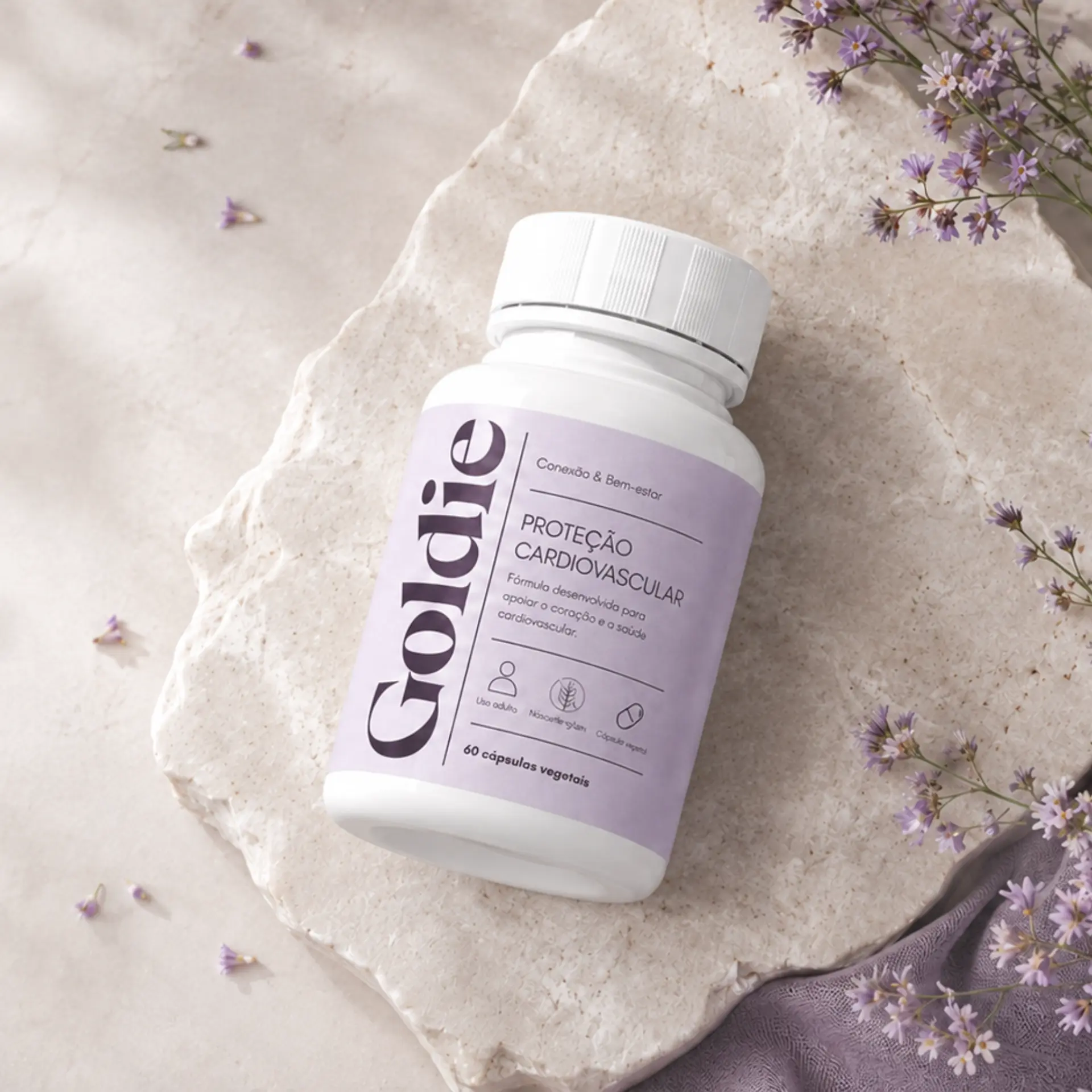 Frasco Goldie Proteção Cardiovascular deitado sobre pedra com flores lilás
